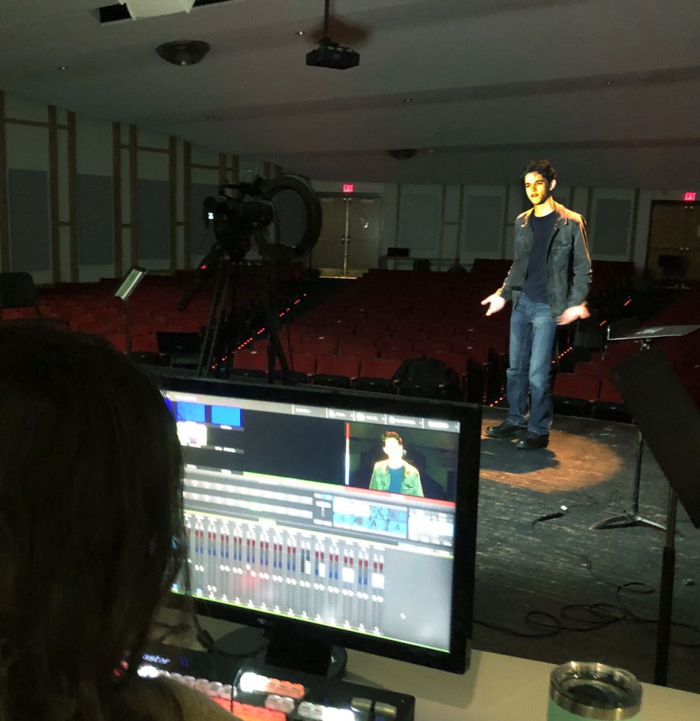 Picture of Student under the spotlight rehearsing the monologue. View from behind a computer screen.