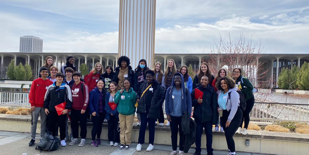 27 GHS students from the upper-level French classes standing outside on the SUNY Albany campus smiling at the camera for a picture.