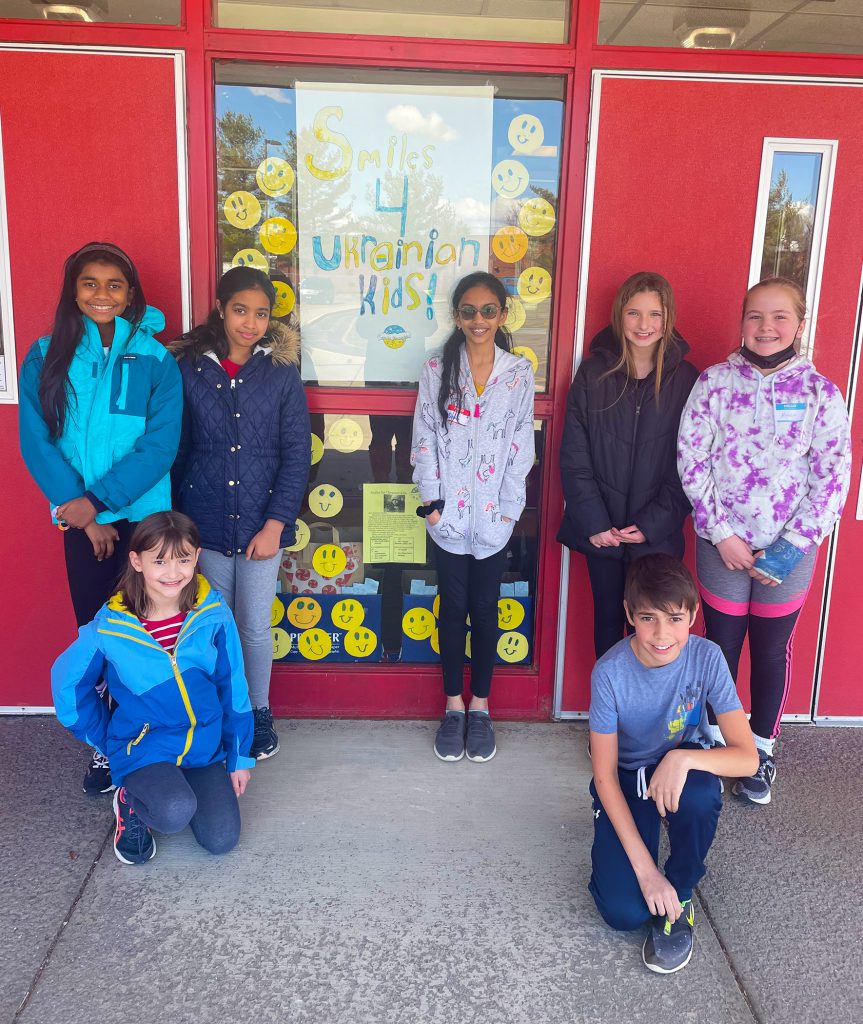 Alyssa Jantzen and her classmates smiling in front of Westmere's entrance that's covered in "Smiles for Ukraine".
