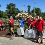 Advisor wearing a red t-shirt speaks to attendees at release ceremony. Behind her are volunteers, with hands raised.