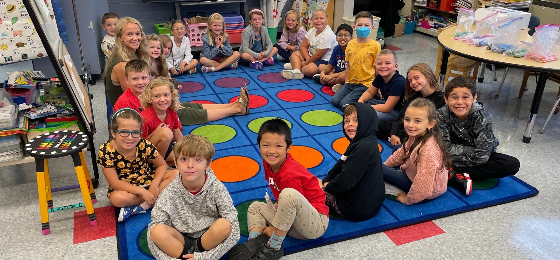 Elementary students in class sitting on reading carpet smiling for the camera