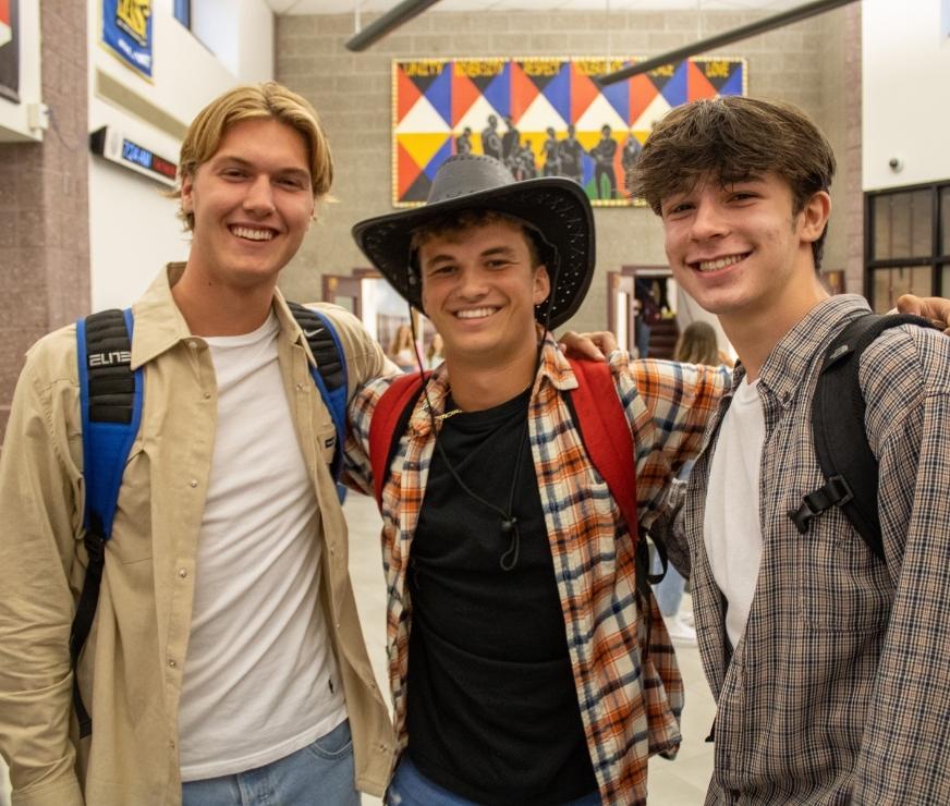 Three students dressed in collared shirts, posing for camera. Student in the middle is wearing a cowboy hat.