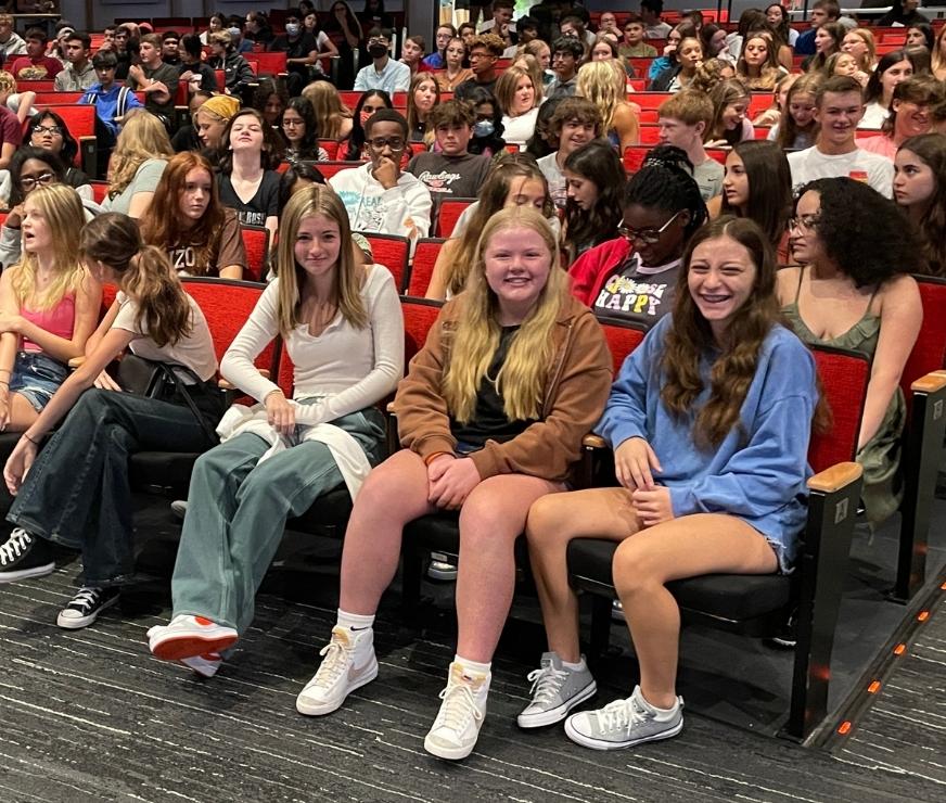 Group of students smile for the camera while sitting in auditorium seats at ninth grade orientation.