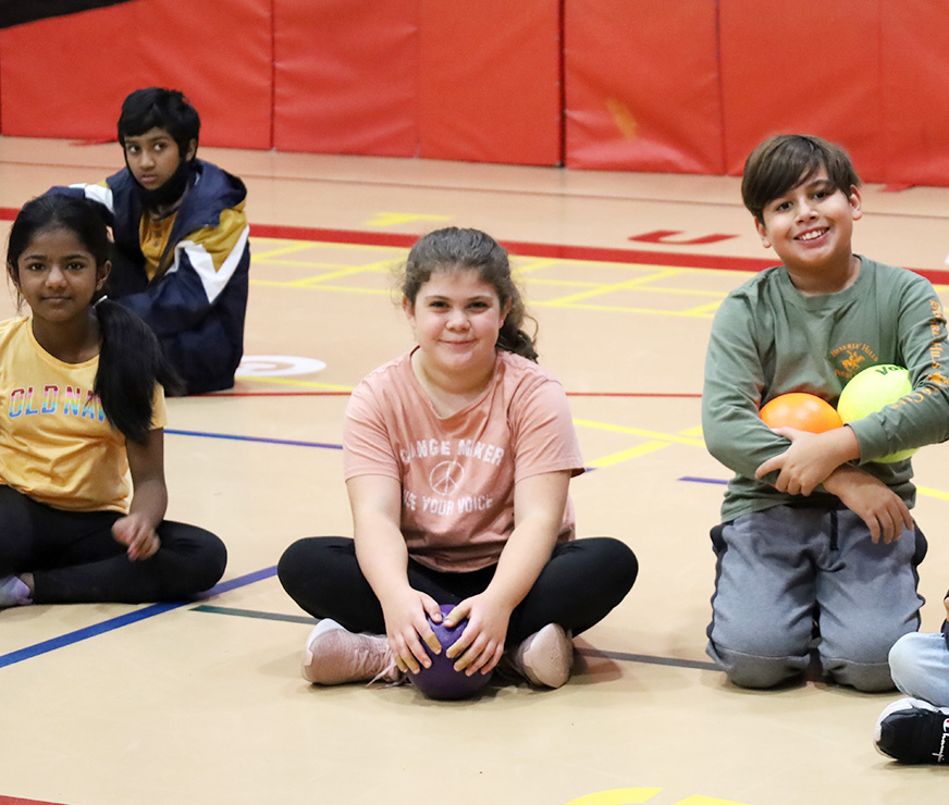 A group of Pinebush Elementary students sitting on the gymnasium floor in PE class.