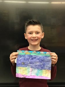 Student holds artwork he created up to the camera