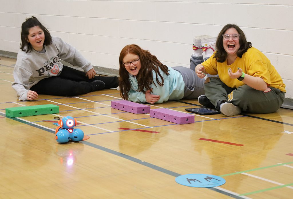 Students smiling as they watch their robot move.