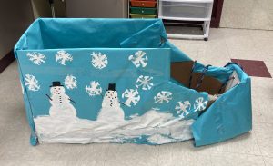 Cardboard sled decorated with blue paper and painted snowmen and snowflakes