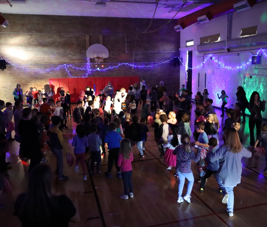 Students dance in the gym with colorful lights glowing off the walls.