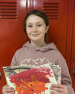 Student stands in front of a red locker, holding artwork.