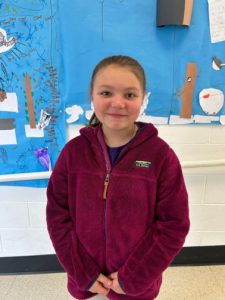 Student stands in front of a bulletin board with student artwork.