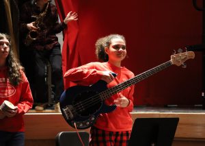 Student, wearing a red t-shirt, holds a bass guitar.
