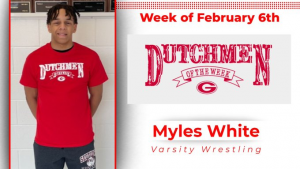 Student is standing in front of white wall wearing a red t-shirt that says Dutchmen of the Week in white letters.
