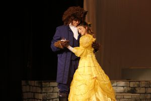 Two students in costume dance during rehearsal for Beauty and the Beast. One is dressed as the beast, one is wearing a yellow dress.