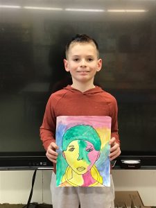 Student holds artwork while standing in front of a blackboard