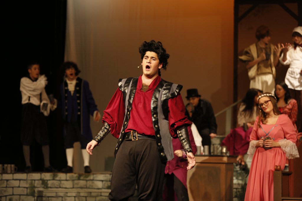 Student signs on stage, rehearsing Beauty and the Beast.