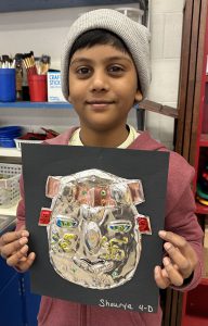 Elementary student holds up artwork he created, smiling at camera.