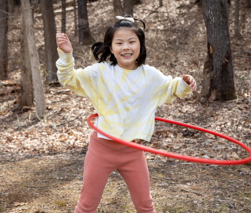 Student in vibrant yellow shirt smiles as they hoola hoop outside on a sunny day.