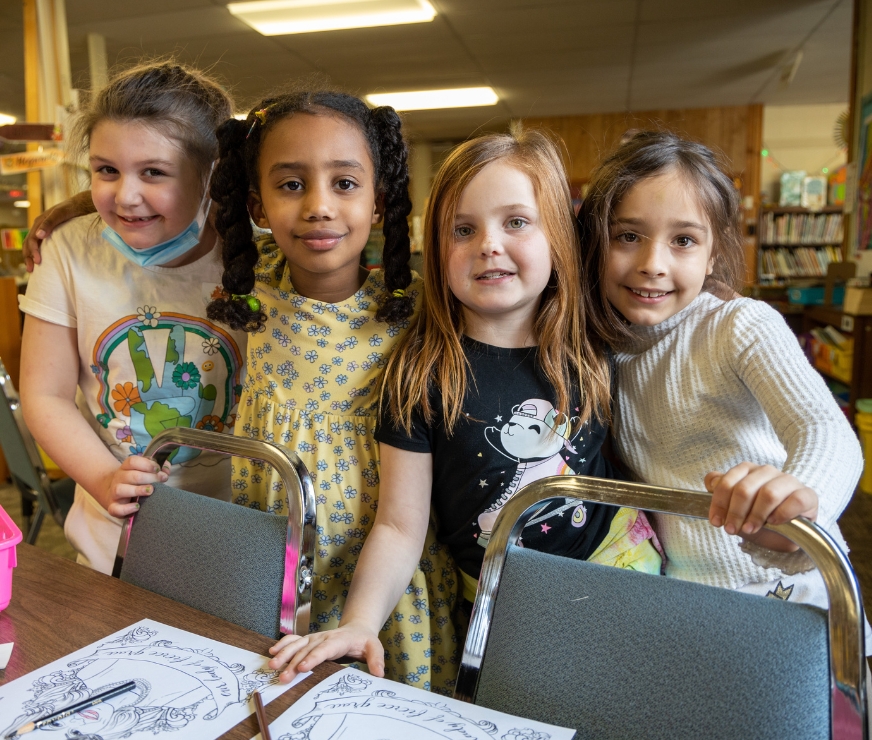 Fours students stand at a table in the library, smiling for a picture.