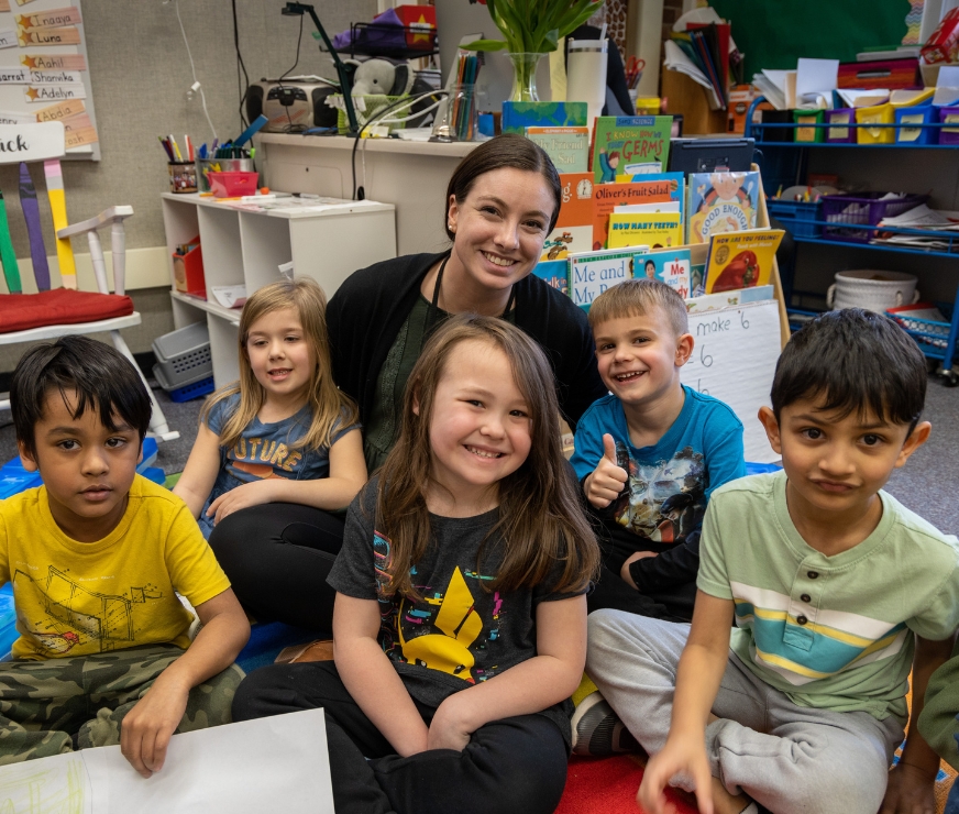 A teacher sits on the floor with students during playtime.