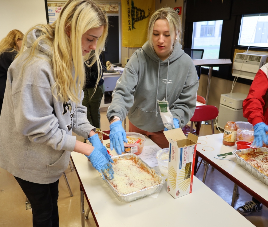 Two students work together a table to prep lasagna.