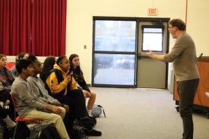 Visiting author Brendan Kiely gestures while speaking to GHS students. In the frame, you can see two rows of students sitting in chairs.