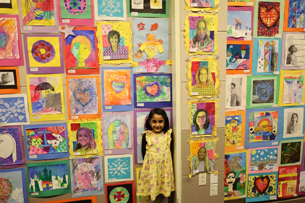 Student stands in front of a wall of colorful artwork.