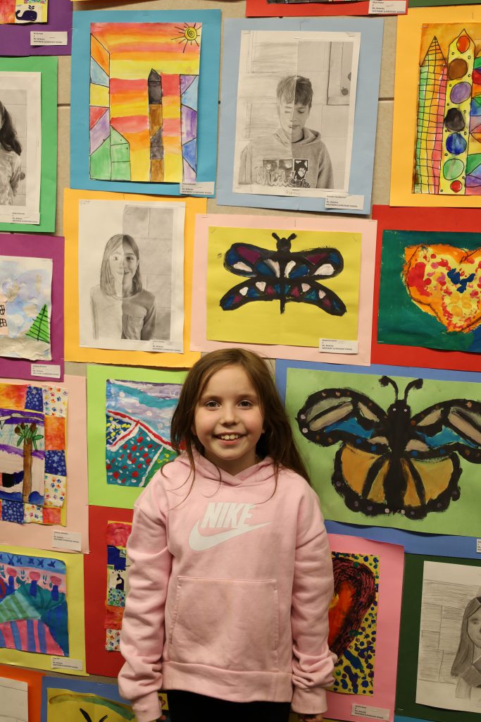 Elementary student stands in front of a wall of colorful artwork.
