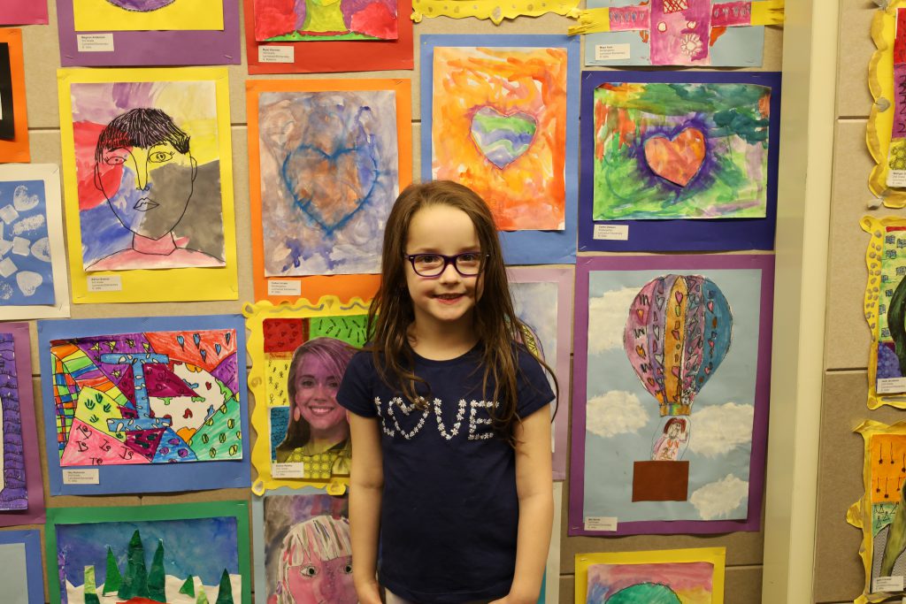 Student stands in front of a wall of colorful artwork.