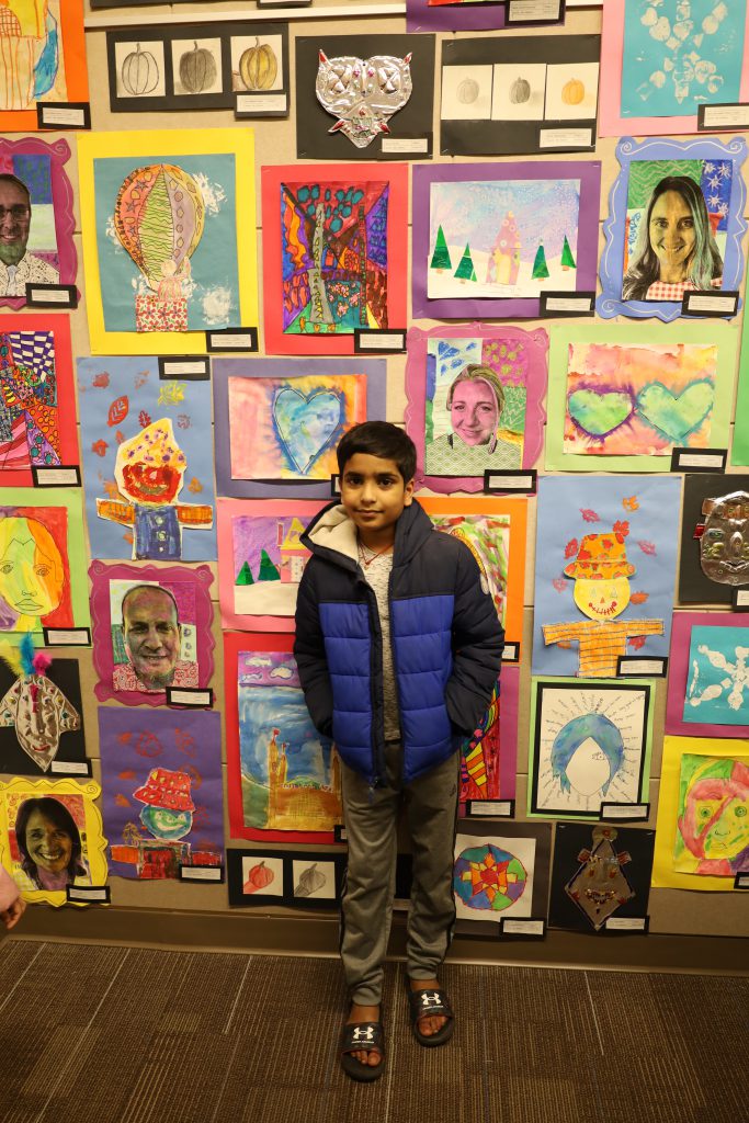 Student stands in front of a wall of colorful artwork.
