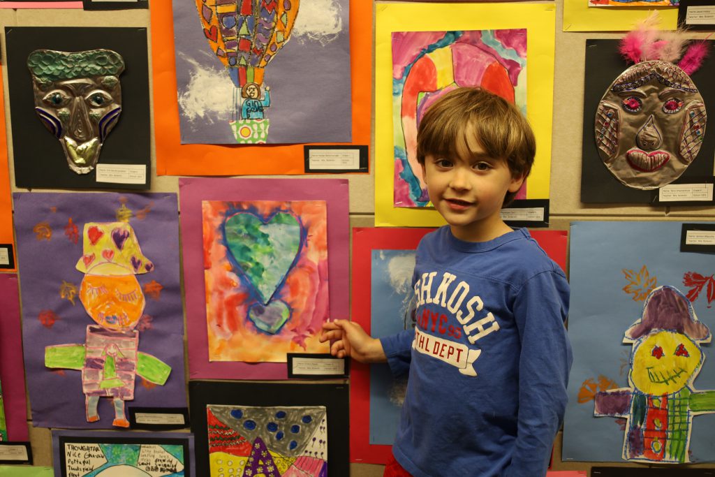 Elementary student points to a piece of artwork he created