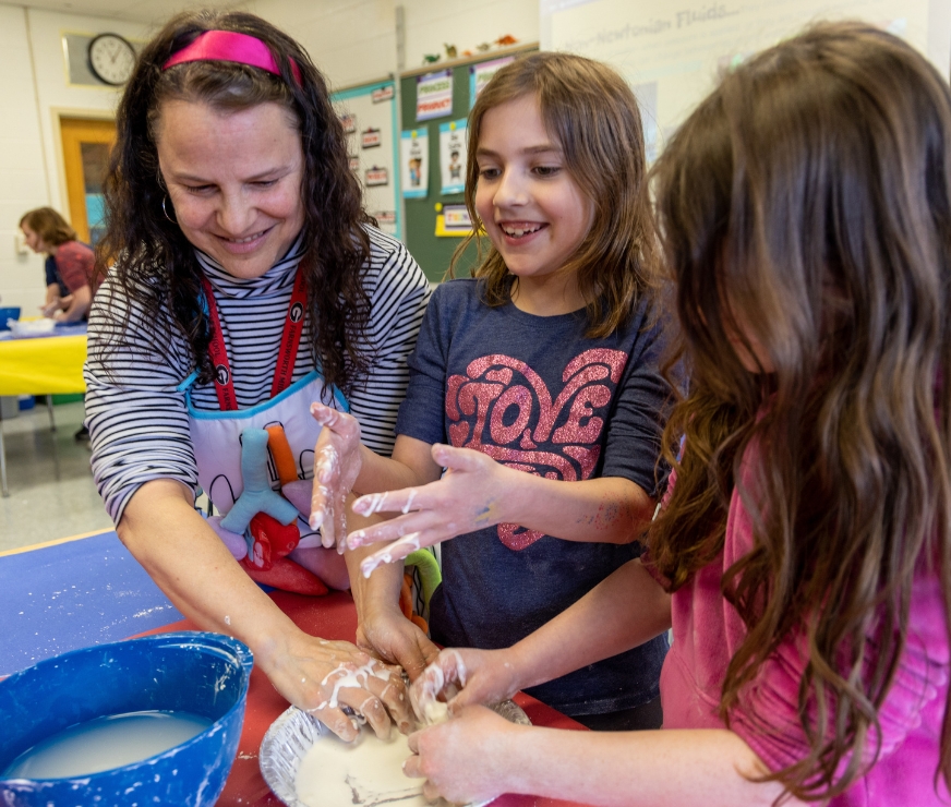 A teacher helps two students with a science lab activity.