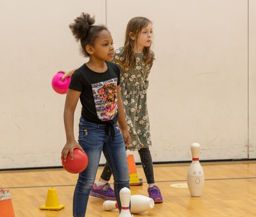 Two students defending bowling pins during a game in physical education class.