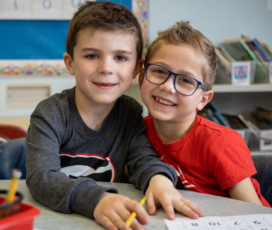 Two students sitting at table smile for the camera.