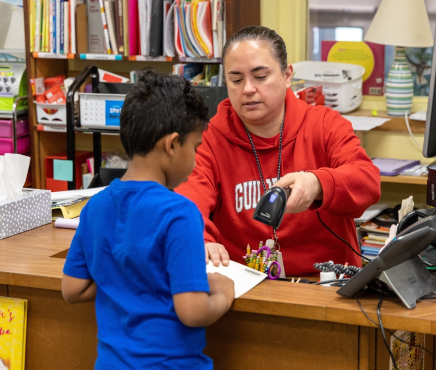 Librarian helps a student check a book out of the library.