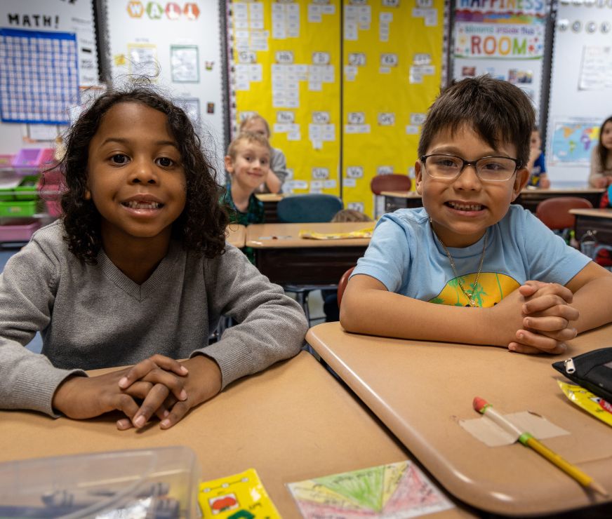 Two students sit at desk and smile for the camera.