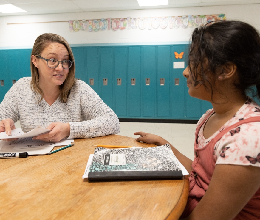 a teacher works with a student one on one at a table in the hallway.