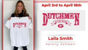 Smiling student stands in front of white wall, holding up a white t-shirt with red text that says: "Dutchmen of the Week"