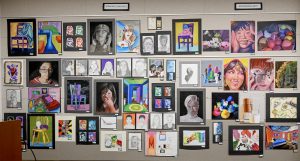 A variety of artwork is displayed on a light tan wall.