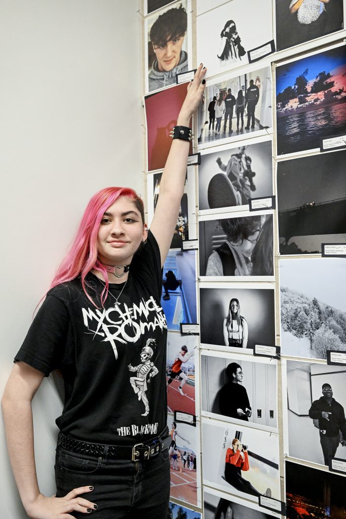 Student points to artwork on a wall where many pieces of artwork are displayed.