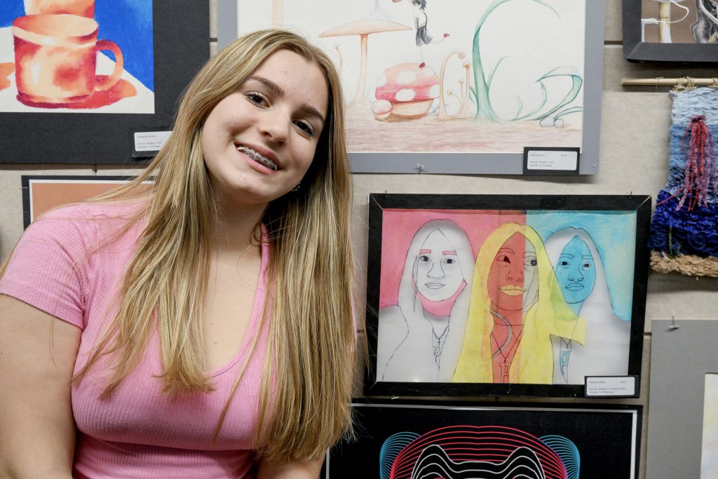 Student smiles next to artwork they created.