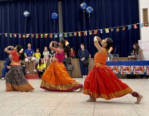 Three LES students wearing brightly colored traditional clothes from their culture dance in the LES gym at the International Night event.
