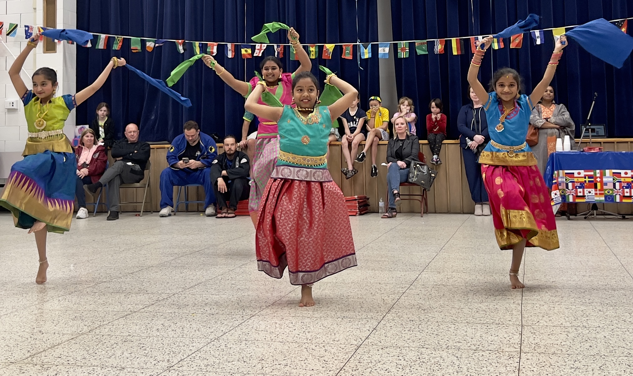 Four LES students wearing brightly colored traditional clothes from their culture dance in the LES gym at the International Night event.