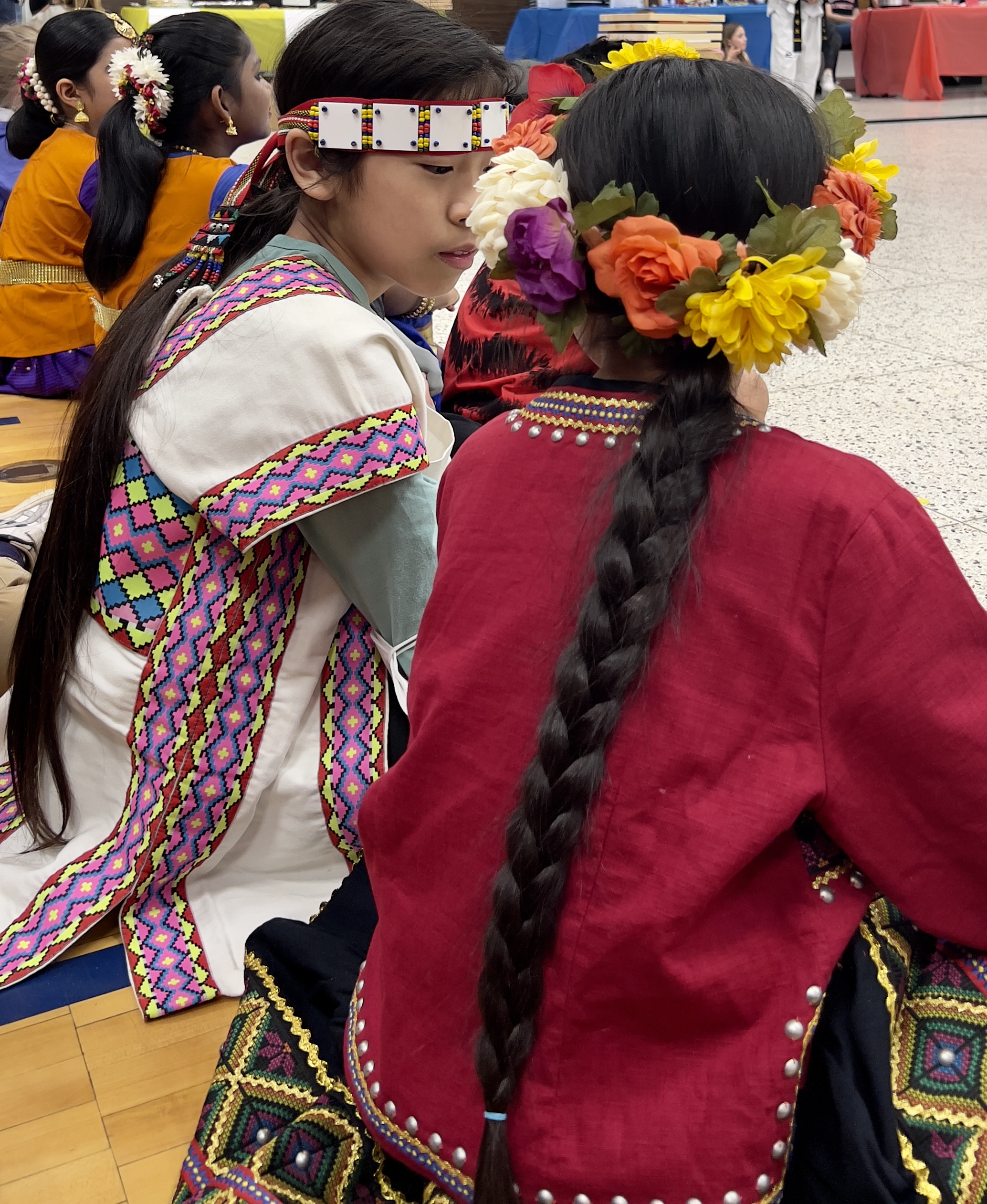Two LES students wearing traditional clothes from their culture sit next to each other at the LES International Night event.