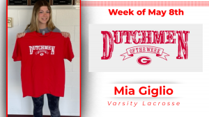 Student stands in front of a while wall, holding a red t-shirt with white type that reads: Dutchmen of the Week
