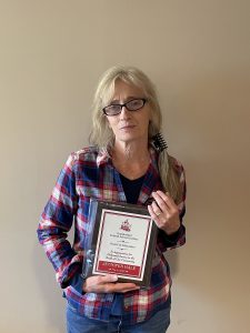 Woman stands in front of a blank wall holding a plaque