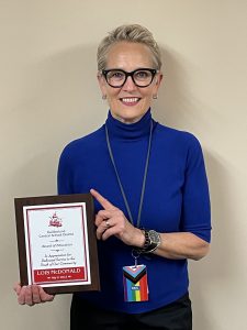 Woman stands in front of a blank wall holding a plaque