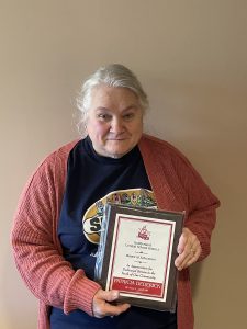 Woman stands in front of a blank wall holding a plaque