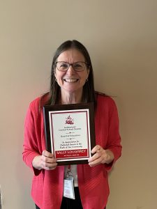 Smiling woman stands in front of a blank wall holding a plaque