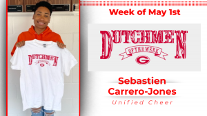 Student stands in front of a white wall, holding a white t-shirt with red text that reads Dutchmen of the Week