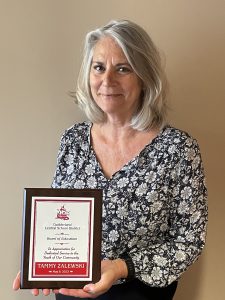 Woman stands in front of a blank wall holding a plaque